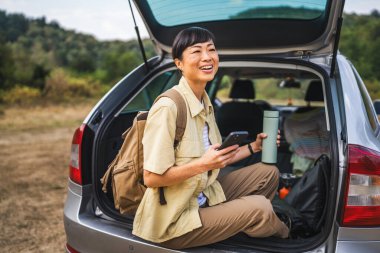 Olgun Japon kadın cep telefonu kullanıyor ve arabasının arkasında oturuyor.