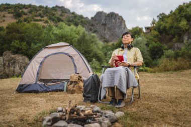 Olgun Japon kadın kamp gezisinde çadırının önünde kitap okudu.