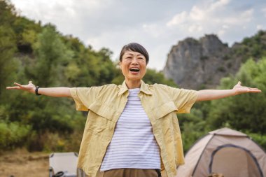 Olgun Japon kadın portresi orman kampı konseptinde bir çadırın önünde duruyor.