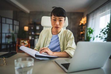 Kulaklık takan olgun Japon kadın laptopta ve panoda çalışıyor.