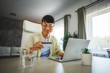 Olgun, mutlu Japon kadın evde kredi kartıyla internetten bilgisayar alıyor.