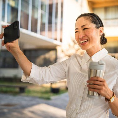 Yetişkin Japon iş kadınının cep telefonundaki oto portresi ya da görüntüsü modern binaların önünde duruyor.
