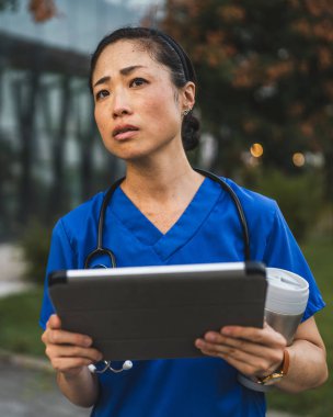 Kafası karışmış yaşlı Japon doktor binanın önünde dur ve dijital tablet kullan.