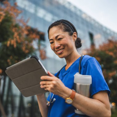 Olgun Japon doktor binanın önünde dur ve dijital tablet kullan.