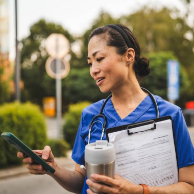 portrait of japanese doctor stand and hold clipboard and mobile phone drink from thermos on the street clipart