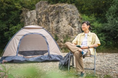 Olgun Japon kadın kamp gezisinde çadırın önüne oturur ve cep telefonu kullanır.