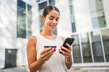 Genç bir kadın binanın önünde duruyor ve kredi kartıyla internetten satın alıyor.