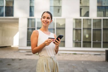 Genç bir kadın binanın önünde duruyor ve kredi kartıyla internetten satın alıyor.