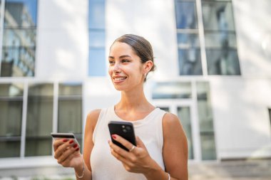 Genç bir kadın binanın önünde duruyor ve kredi kartıyla internetten satın alıyor.