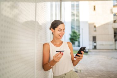 Genç bir kadın binanın önünde duruyor ve kredi kartıyla internetten satın alıyor.