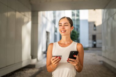 Genç bir kadın binanın önünde duruyor ve kredi kartıyla internetten satın alıyor.