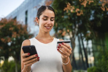 Genç kadın inşaat şirketinin önünde duruyor ve kredi kartıyla cep telefonundan satın alıyor.
