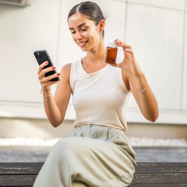 Young woman use mobile phone for read instruction for pills, tablets in front building clipart