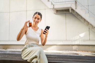 Young woman use mobile phone for read instruction for pills, tablets in front building clipart