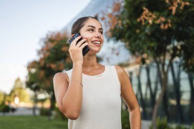Açık hava şirketinde cep telefonuyla konuşan genç bir kadının portresi.