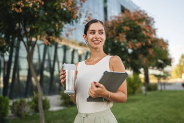 Genç bir kadının portresi şirketin önünde duruyor ve dijital tablet kullanıyor.