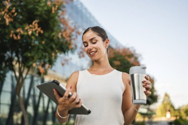 Genç bir kadının portresi şirketin önünde duruyor ve dijital tablet kullanıyor.