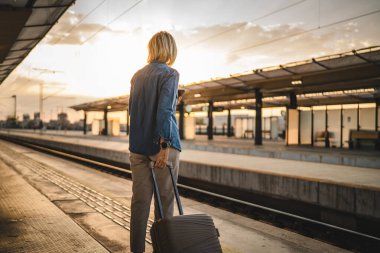 Yetişkin bir kadının arkası. Tren istasyonunda bekle, cep telefonunu ve bavulunu tut.