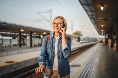 Olgun kadın treni bekle ve beklerken cep telefonuyla konuş.