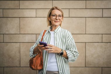 Mutlu yetişkin kadın portresi beyaz duvarın önünde dur ve cep telefonu kullan