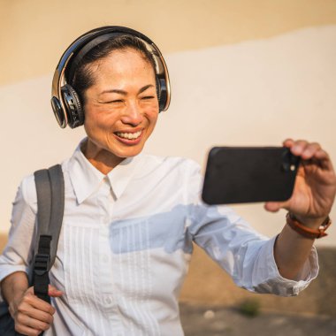 Yetişkin Japon iş kadınının cep telefonundaki oto portresi ya da görüntüsü dışarıda duruyor.