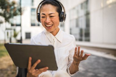 Kulaklıklı olgun Japon kadın dijital tablette video çağrısı yapıyor.