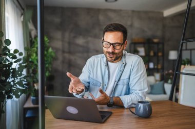 Yetişkin beyaz adam evde çalışıyor ve bilgisayarında video görüşmesi yapıyor.