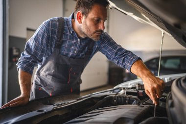 Yetişkin adam araba tamircisi garajda çalışıyor, araç kaputu açıkken araç tamir etmek için aletler kullanın, motorun iyi durumda olduğundan emin olmaya odaklanın.