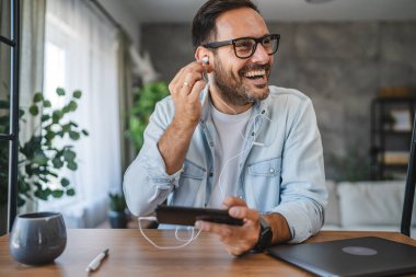 Gözlüklü mutlu bir adam cep telefonu ve kulaklıkla müzik dinliyor.