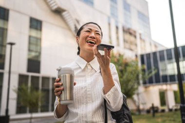 Olgun Japon iş kadını işten önce modern binaların önünde sesli mesaj ya da ses tanıma sistemi kurar.