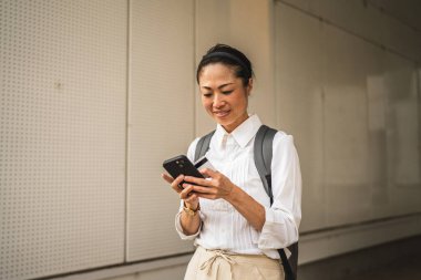 Olgun Japon kadın açık hava kredi kartıyla cep telefonundan online alışveriş yapıyor.