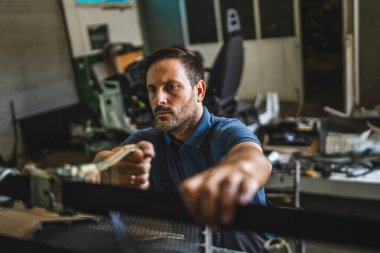 Yetişkin adam araba tamircisi yoğun bir şekilde çeşitli ekipmanlarla dolu yoğun bir atölyede çalışıyor, bir zanaatçının ortamında odaklanma ve kararlılık gösteriyor