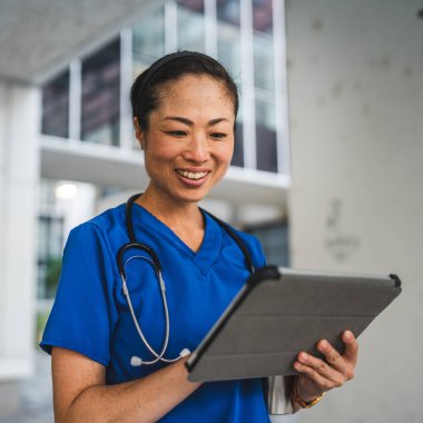 Olgun Japon doktor binanın önünde dur ve dijital tablet kullan.