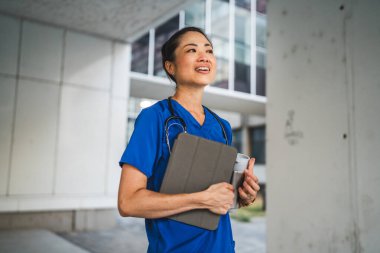 Olgun Japon doktor binanın önünde dur ve dijital tablet kullan.