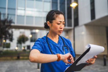 Meşgul yetişkin Japon doktor, panoyu tutarken dur ve zamanı kontrol et.