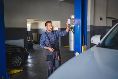 Araba tamircisi araba tamircisinin lastiklerini kontrol etmek için araba kaldırma ayarı yapıyor.