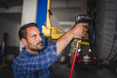 Bir araba tamircisi, bir otomotiv tamirhanesinde araç kaldırılırken veya değiştirildiğinde hassas bir işe odaklanırken, elektrikli bir araç kullanır.