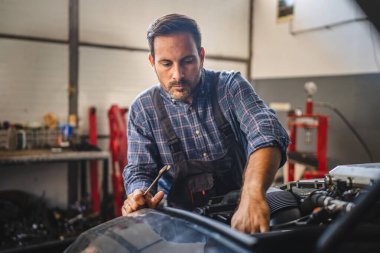 Adanmış bir araba tamircisi otomotiv atölyesindeki bir araba motoru üzerinde dikkatle çalışır, becerikli bir elden tamir uzmanlığı gösterir ve odaklanır.