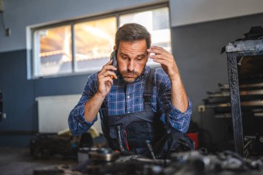 kafası karışmış tamirci araba motorunu garajda araç gereçle kontrol et ve cep telefonuyla konuş