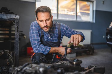 Bir araba tamircisi bir garajın içindeki araba motorunu kontrol eder, bakım ve onarım işine odaklanır. Görüntü detaylara ve teknik uzmanlığa dikkat çeker.