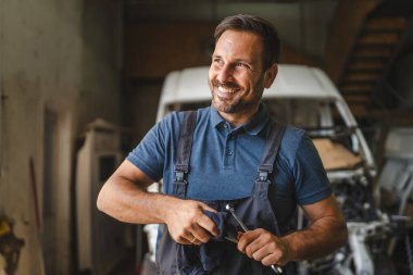 Araba tamircisi arka planda açık motorlu temiz giysiler tutuyor.