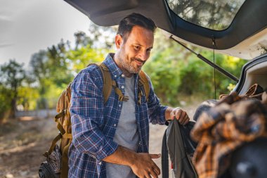 Yetişkin adam bagajdan çantasını alıp ormanda yeni bir maceraya hazır olsun.