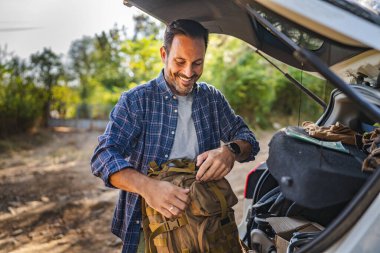 Yetişkin adam bagajdan çantasını alıp ormanda yeni bir maceraya hazır olsun.