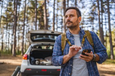 Yetişkin kampçı ormanda ön vagonda cep telefonu kullanıyor.