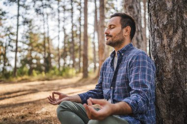 Yetişkin adam kampçısı meditasyon yapıyor ve ön ağaçta nefes egzersizi yapıyor.