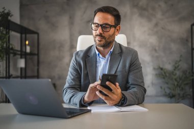 Hüsnükuruntulu işadamı masada oturur ve modern ofiste cep telefonunu kullanır.