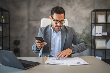 İşadamı ofisinde oturuyor ve cep telefonundan ödenmemiş faturalar alıyor.