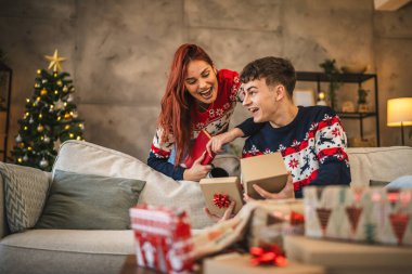 Kız arkadaşı konuşur ve erkek arkadaşına destek olur. O da Noel hediyesini evdeki kanepeye sarar.