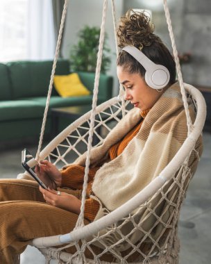 Genç bir kadın evde oturup dijital tablet ve kulaklık kullanarak film ya da dizi izlemek ya da mutlu bir gülümseme görüntüsü almak için iyi vakit geçirin.