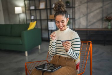 Yetişkin beyaz bir kadın mutlu bir şekilde gülümseyerek evde oturuyor banka kredi kartlarını online alışveriş konseptinde tutuyor gerçek insanlar uzay e-ticaretini kopyalıyor ya da rezervasyon yaptırıyor.